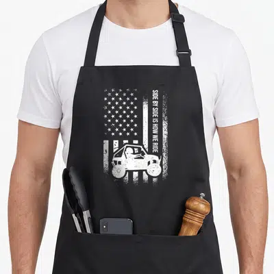 Ride american flag apron - Distressed white USA flag background with vertical text and UTV silhouette — shown on a black cotton canvas apron against a white background