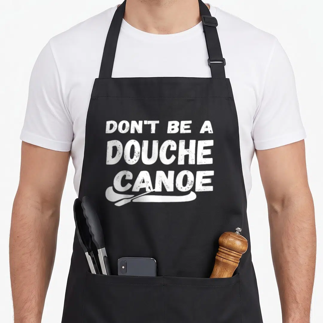 Douche canoe apron - White distressed text Don't Be A Douche Canoe with paddle graphic below — shown on a black cotton canvas apron against a white background