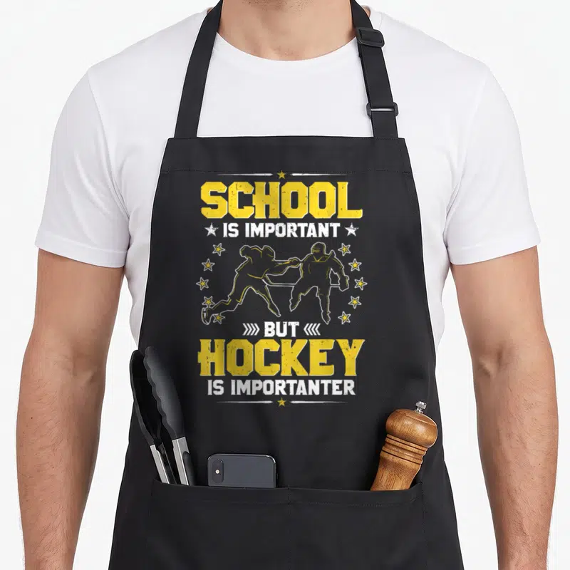 School hockey humor apron - Two hockey players skating between yellow and white distressed text reading School Is — shown on a black cotton canvas apron against a white background