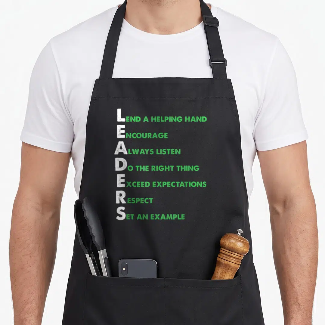 Lead boss apron - Green and white acrostic poem for LEADERS with inspirational phrases on black fabric — shown on a black cotton canvas apron against a white background