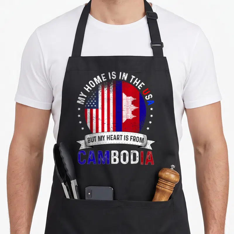 Cambodian patriot american flag apron - Distressed circular emblem with US and Cambodia flags andMY HOME IS IN THE USA — shown on a black cotton canvas apron against a white background