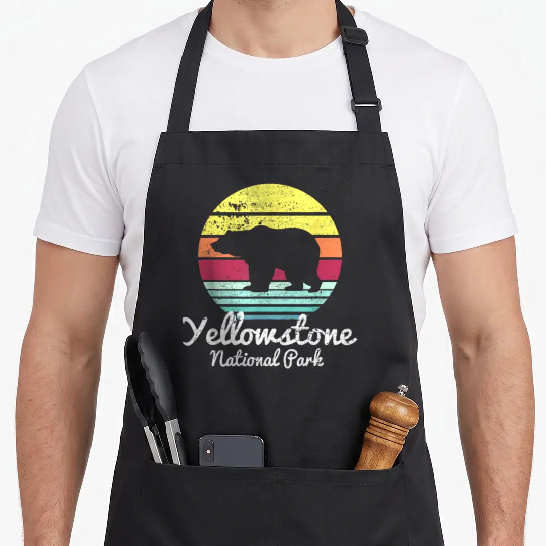 Park wyoming bear apron - Grey bear silhouette over striped retro sun with Yellowstone National Park text — shown on a black cotton canvas apron against a white background