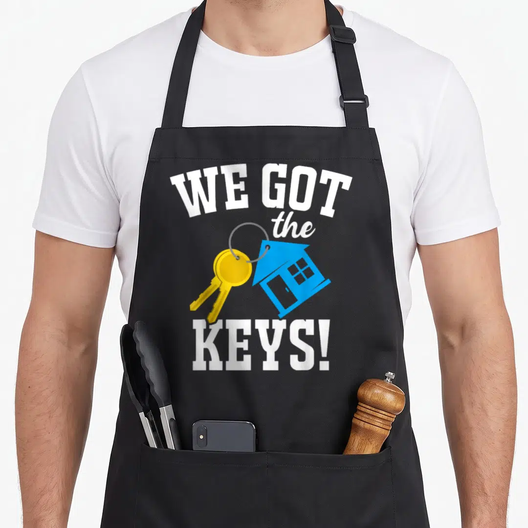 Bought key homeowner apron - Arched WE GOT the KEYS text with yellow keys and blue house icon — shown on a black cotton canvas apron against a white background