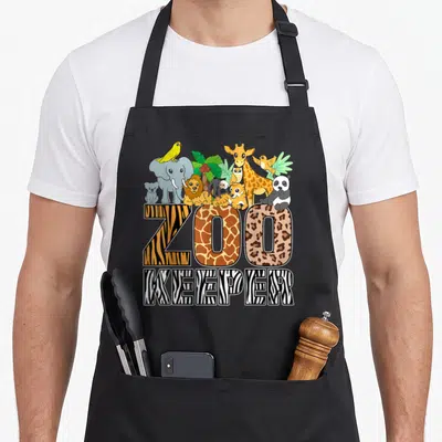 Costume zebra apron - ZOO KEEPER text with tiger giraffe leopard patterns and cartoon animals — shown on a black cotton canvas apron against a white background