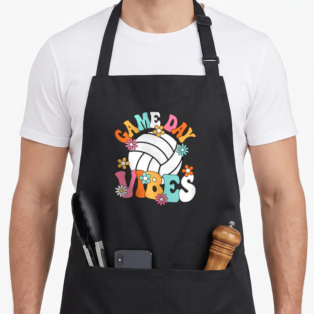 Vintage volleyball game aprons - Cartoon volleyball with GAME DAY VIBES text and pink orange blue yellow flowers — shown on a black cotton canvas apron against a white background