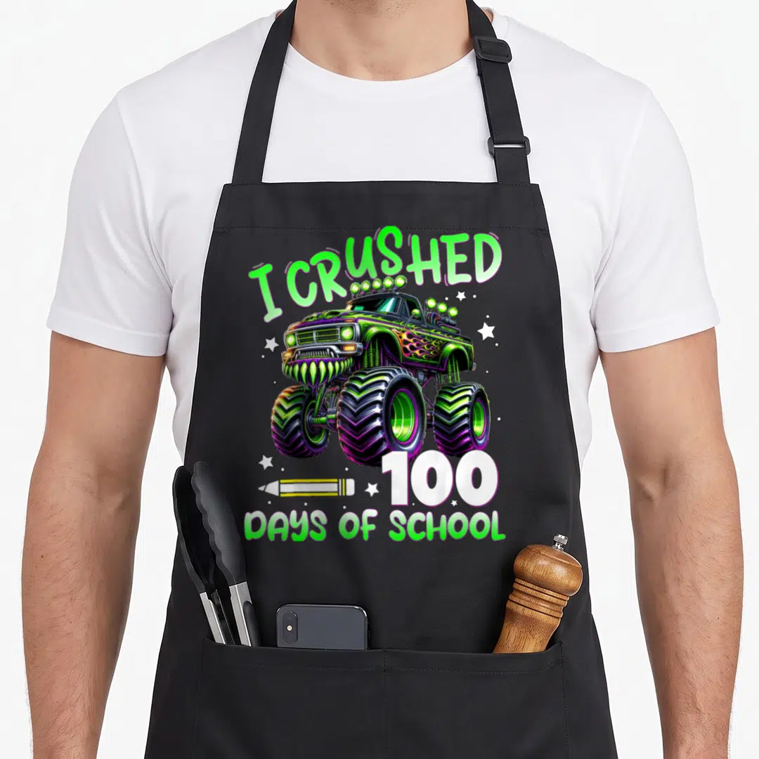 100th truck apron - I Crushed 100 Days of School monster truck with pencil and stars in green purple white yellow — shown on a black cotton canvas apron against a white background
