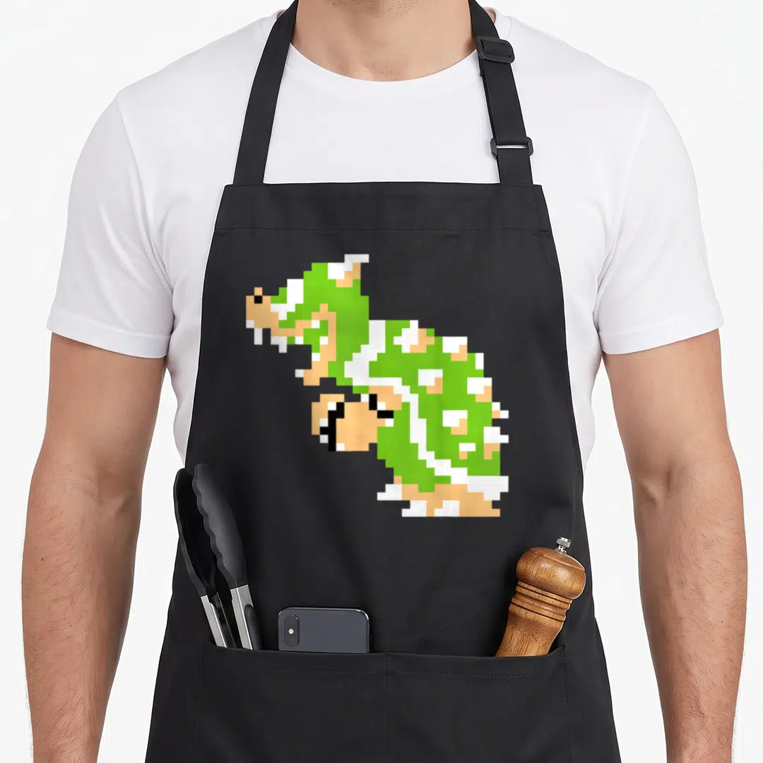 Bit holiday apron - Green pixel art Koopa Troopa sprite centered on canvas — shown on a black cotton canvas apron against a white background