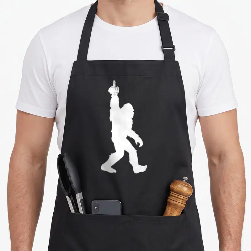 Middle bigfoot apron - White Bigfoot silhouette raising one finger on black apron — shown on a black cotton canvas apron against a white background