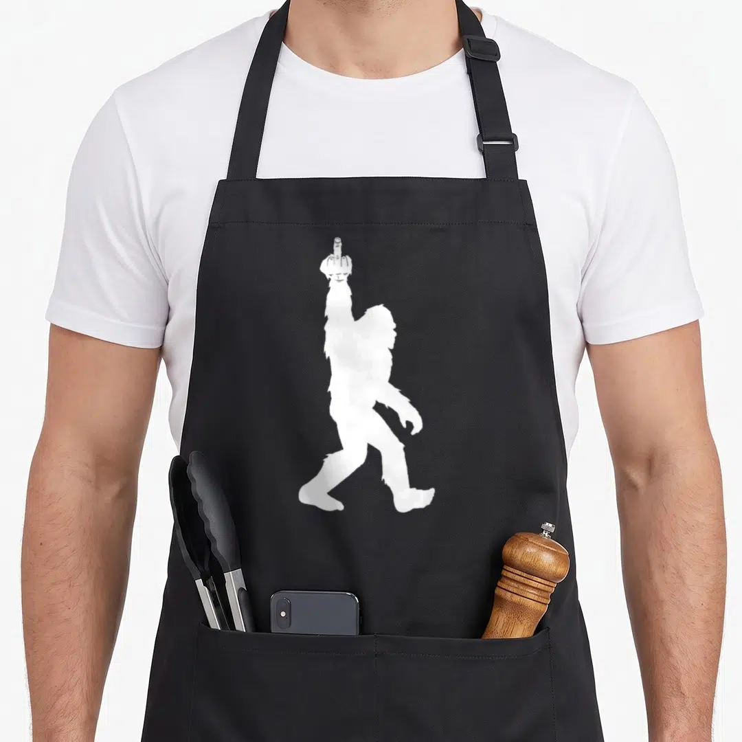 Middle bigfoot apron - White Bigfoot silhouette raising one finger on black apron — shown on a black cotton canvas apron against a white background