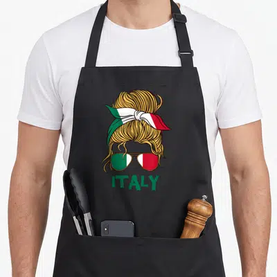 Italy italian aprons - Gold messy bun with Italian flag headband and sunglasses above green ITALY text — shown on a black cotton canvas apron against a white background