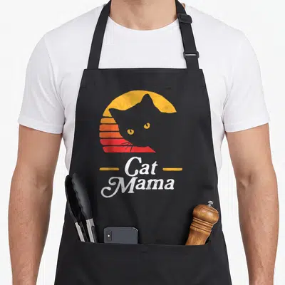 Mama cat apron - Grey cat silhouette over retro striped sun with Cat Mama text — shown on a black cotton canvas apron against a white background