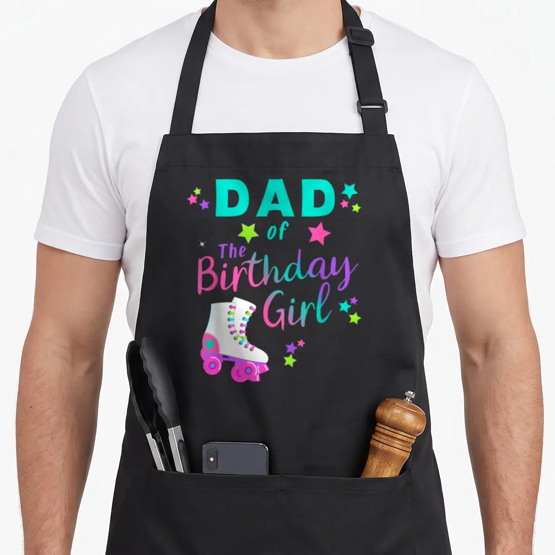 Skate family aprons - DAD of The Birthday Girl text with cartoon roller skate and multicolored stars — shown on a black cotton canvas apron against a white background