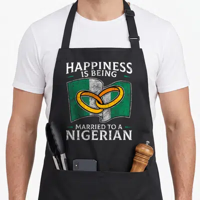 Nigerian wedding apron - Distressed Nigerian flag with two interlocking gold rings and white text reading Happiness Is — shown on a black cotton canvas apron against a white background