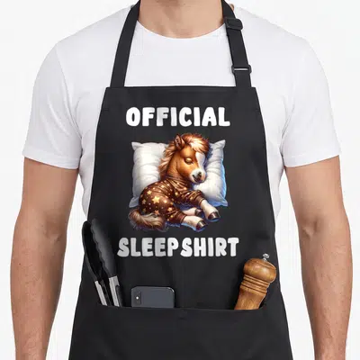 Sleepshirt horse apron - Sleeping brown horse in star pajamas on white pillow with official sleepshirt text — shown on a black cotton canvas apron against a white background
