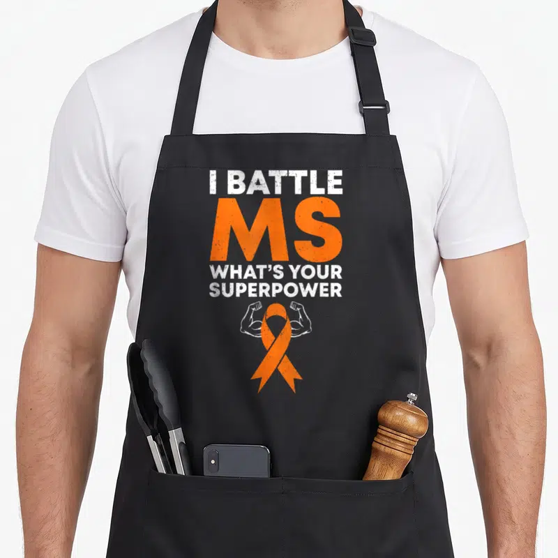 Battle ribbon apron - I Battle MS text above orange ribbon flanked by two white flexed arms — shown on a black cotton canvas apron against a white background