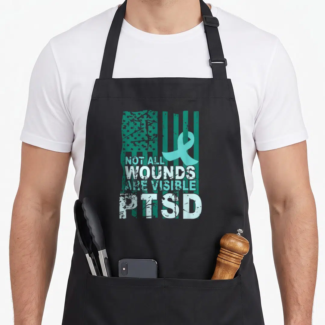 Wound ribbon apron - Teal ribbon and distressed US flag with Not All Wounds Are Visible PTSD text — shown on a black cotton canvas apron against a white background