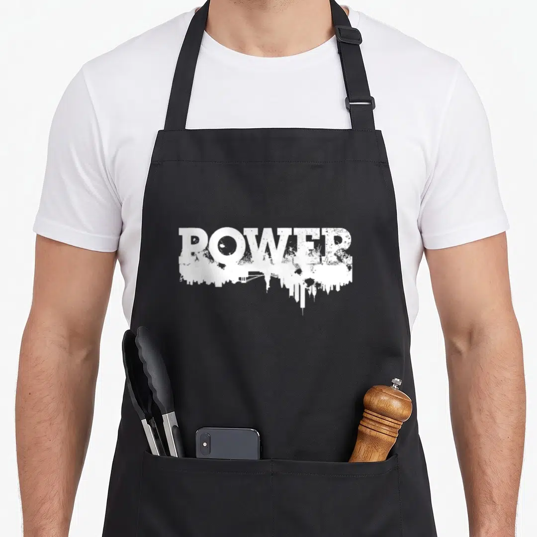 Season power forward apron - Distressed white POWER text with city skyline silhouette integrated into letter bases — shown on a black cotton canvas apron against a white background