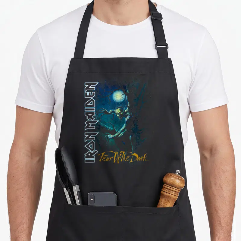 Dark fear apron - Vertical IRON MAIDEN text beside a green monster surrounded by branches and a moon — shown on a black cotton canvas apron against a white background