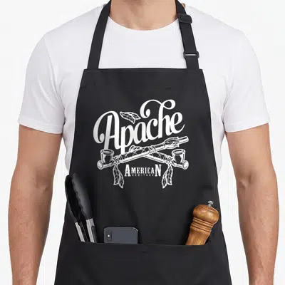 Apache native american aprons - White line art of crossed peace pipes and feathers with text Apache American Heritage — shown on a black cotton canvas apron against a white background