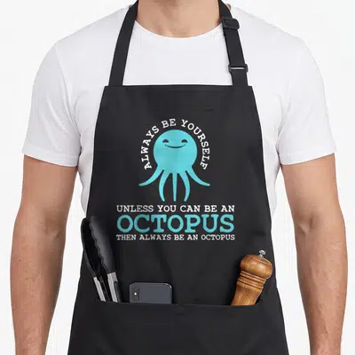 Squid cute octopus and apron - Light blue cartoon octopus with white and blue text reading ALWAYS BE YOURSELF UNLESS — shown on a black cotton canvas apron against a white background