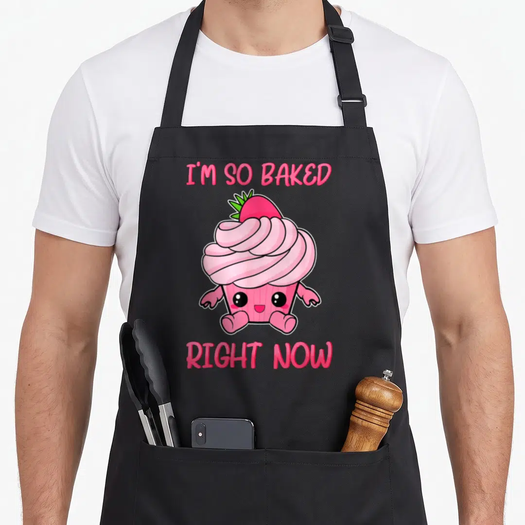 Baked cupcake apron - Pink cartoon cupcake with strawberry and text I'M SO BAKED, RIGHT NOW — shown on a black cotton canvas apron against a white background