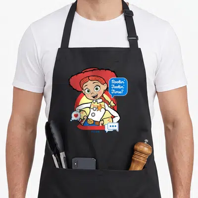 Jessie the story of the apron - Cartoon cowgirl with red hat and blue speech bubble saying Rootin Tootin Time — shown on a black cotton canvas apron against a white background