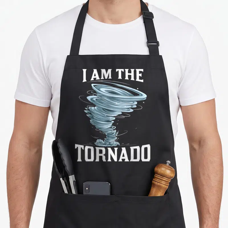 Meteorologist tornado apron - Blue cartoon tornado graphic between white 'I AM THE TORNADO' text on grey background — shown on a black cotton canvas apron against a white background