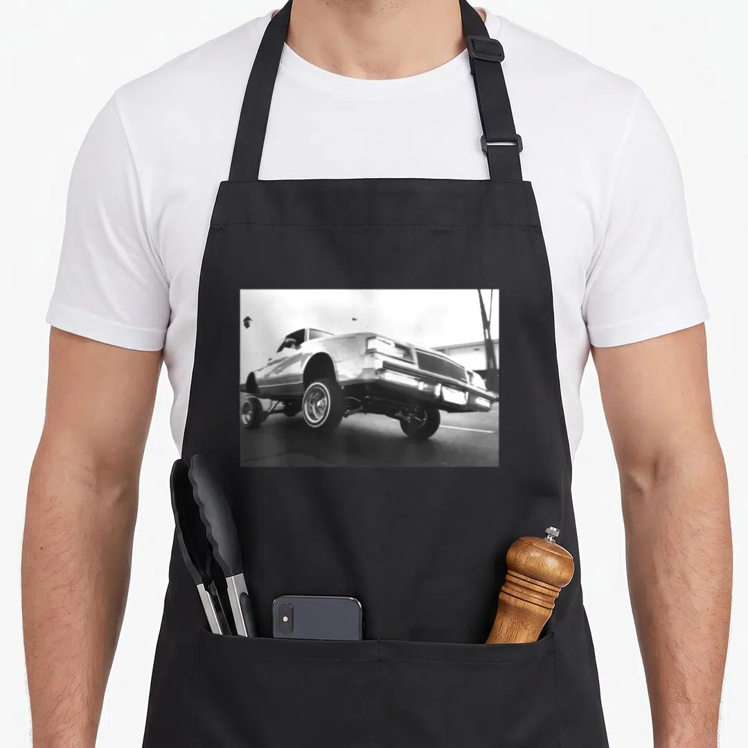 Lowrider wheel apron - Black and white photo of a modified car raised on hydraulics with wire wheels — shown on a black cotton canvas apron against a white background