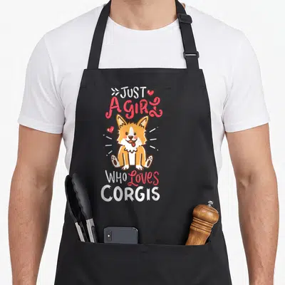 Corgis corgi apron - Cartoon corgi sitting with stacked text Just A Girl Who Loves Corgis and two hearts — shown on a black cotton canvas apron against a white background
