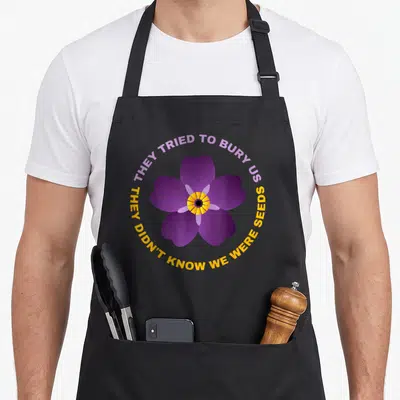 Forget armenian apron - Purple five-petaled flower with yellow center surrounded by circular text on gray background — shown on a black cotton canvas apron against a white background