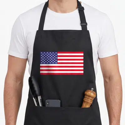 Funny american flag apron - Realistic red white and blue American flag design with two front pockets — shown on a black cotton canvas apron against a white background