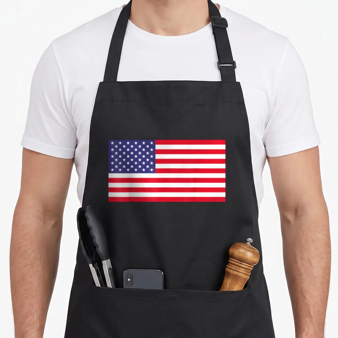 Funny american flag apron - Realistic red white and blue American flag design with two front pockets — shown on a black cotton canvas apron against a white background