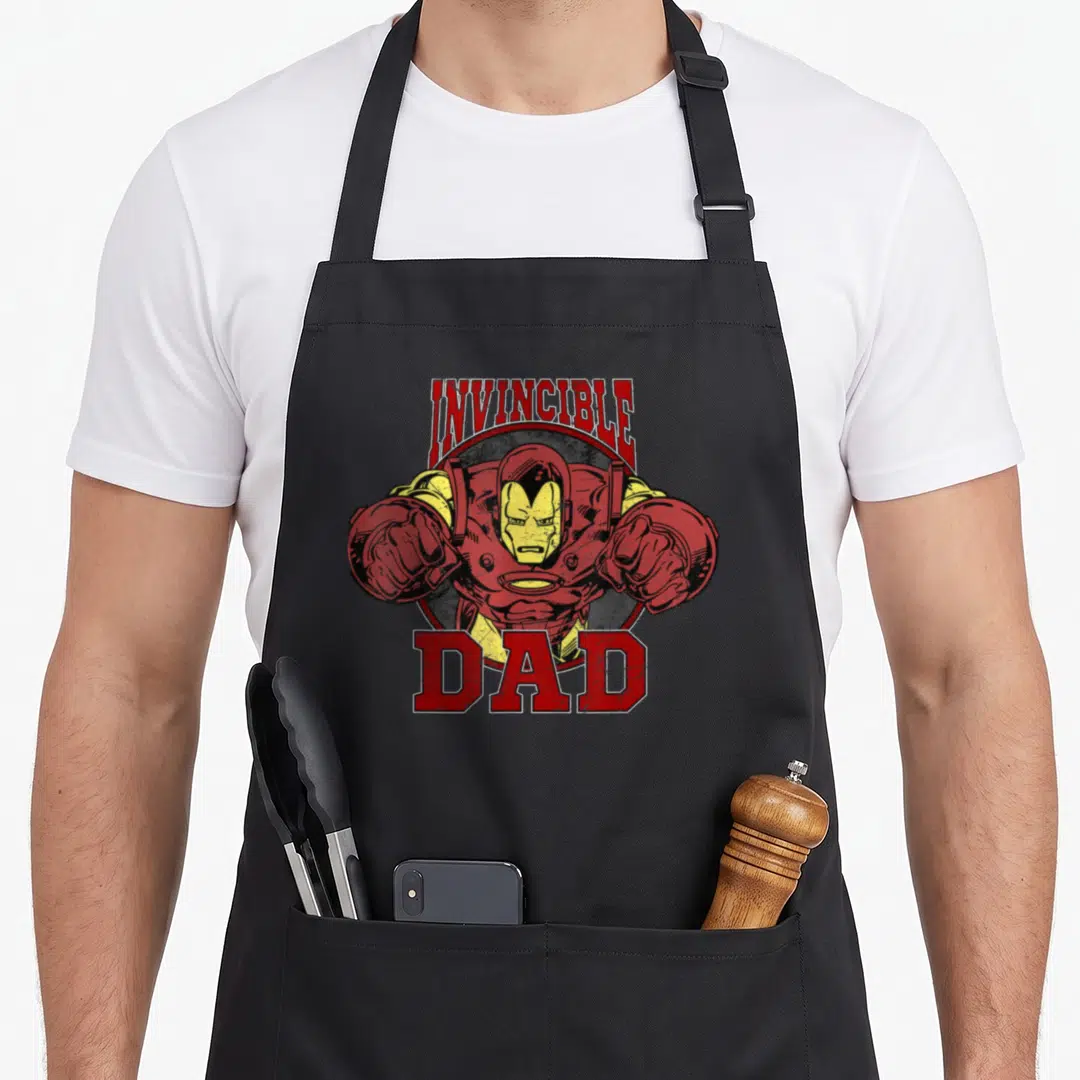 Cool family father day apron - Iron Man upper body punching forward with Invincible Dad text in red gold and black — shown on a black cotton canvas apron against a white background