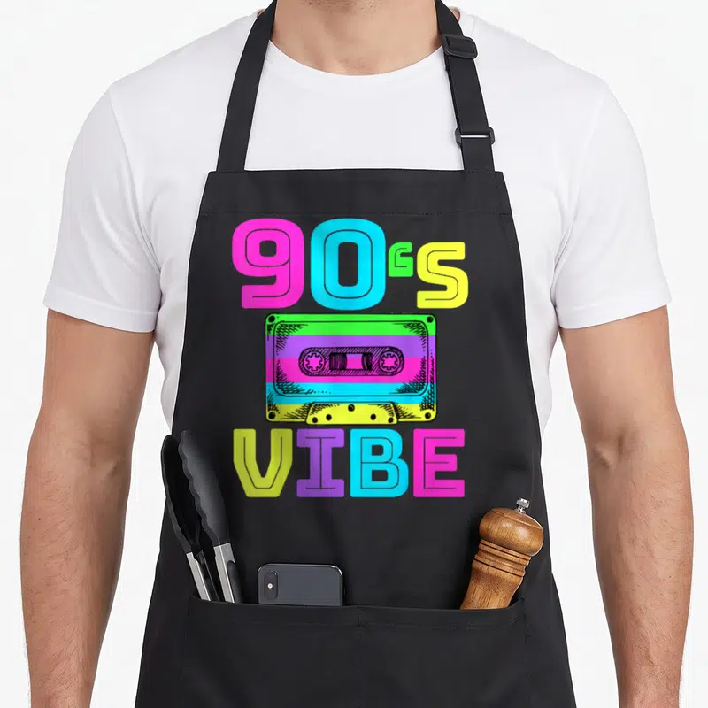 Music 90s apron - Colorful cassette tape with 90s VIBE text in pink blue yellow green purple retro style — shown on a black cotton canvas apron against a white background