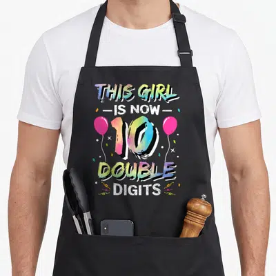 Vintage double birthday apron - Rainbow 10 text with pink balloons and confetti celebrating 10th birthday milestone — shown on a black cotton canvas apron against a white background