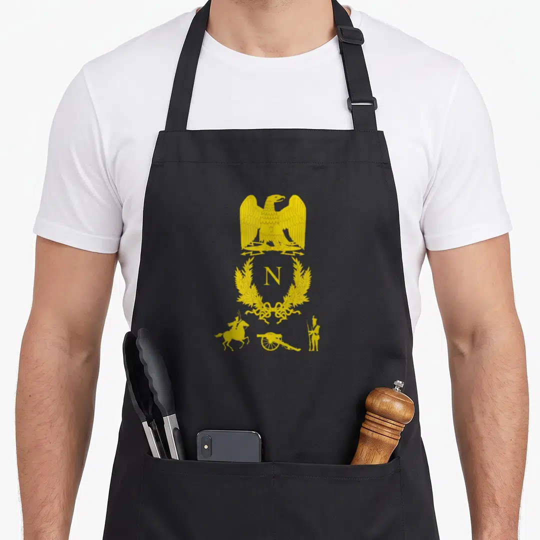 Emblem military apron - Gold eagle and letter N in laurel wreath above cannon and soldiers — shown on a black cotton canvas apron against a white background