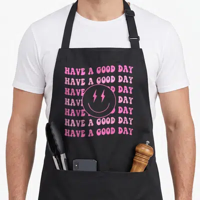 Preppy face on apron - Pink retro smiley face with lightning eyes over seven lines of stacked text — shown on a black cotton canvas apron against a white background