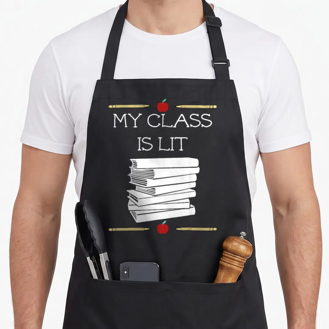 Lit teacher apron - My Class Is Lit text, stack of books, pencils, and red apples in cartoon style — shown on a black cotton canvas apron against a white background