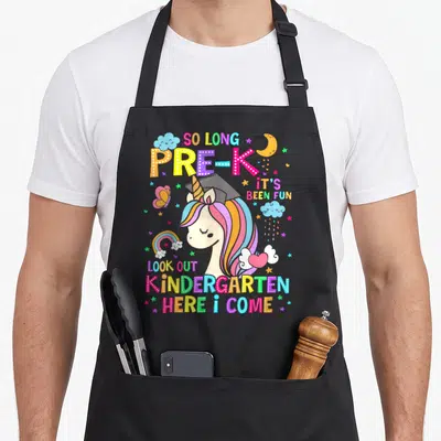 Pre graduation unicorn aprons - Cartoon unicorn with rainbow mane and graduation cap surrounded by stars and text So — shown on a black cotton canvas apron against a white background
