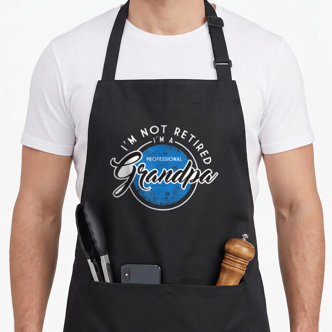 Retired grandpa professional apron - I'M NOT RETIRED text over blue circle with Grandpa script font — shown on a black cotton canvas apron against a white background