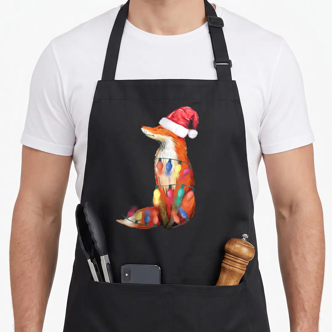 Fox christmas lights apron - Watercolor fox in red santa hat wrapped in blue yellow and red christmas lights — shown on a black cotton canvas apron against a white background