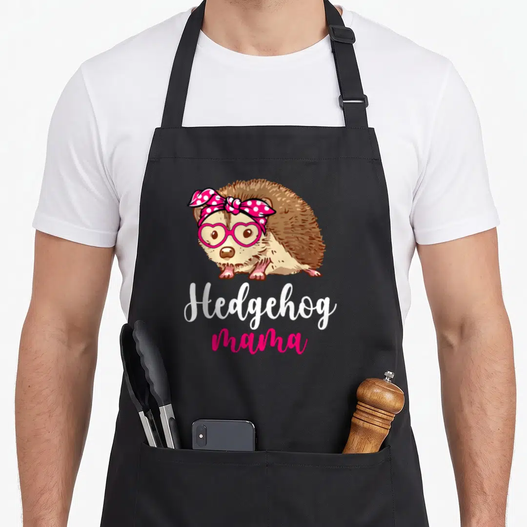 Funny hedgehog mama apron - Cartoon hedgehog in pink glasses and scarf above white and pink Hedgehog mama text — shown on a black cotton canvas apron against a white background