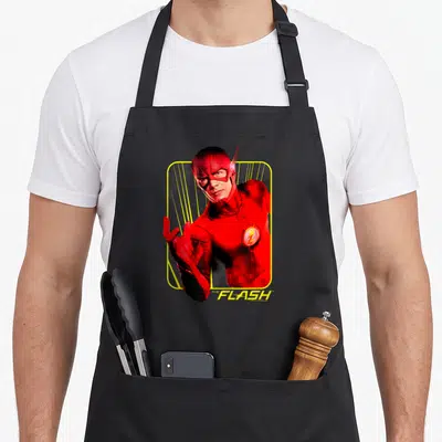 Flash spinning apron - Photo of The Flash in red suit inside yellow rounded frame with speed lines and title text — shown on a black cotton canvas apron against a white background