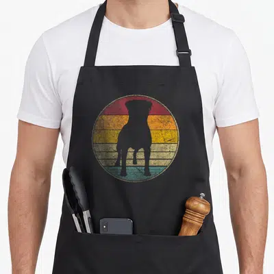 Silhouette dog apron - Grey dog silhouette inside circular sunset with red orange yellow blue grey stripes — shown on a black cotton canvas apron against a white background