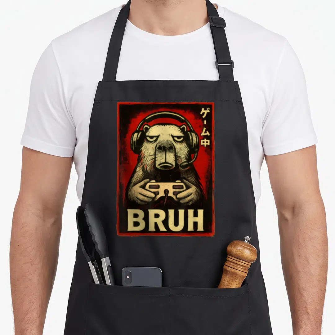Capybara gaming apron - Beige otter with headphones and controller on red background with BRUH text and vertical — shown on a black cotton canvas apron against a white background