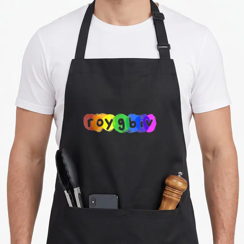 Roygbiv paint apron - Printed roygbiv text over red, orange, yellow, green, blue, indigo, violet paint splashes — shown on a black cotton canvas apron against a white background