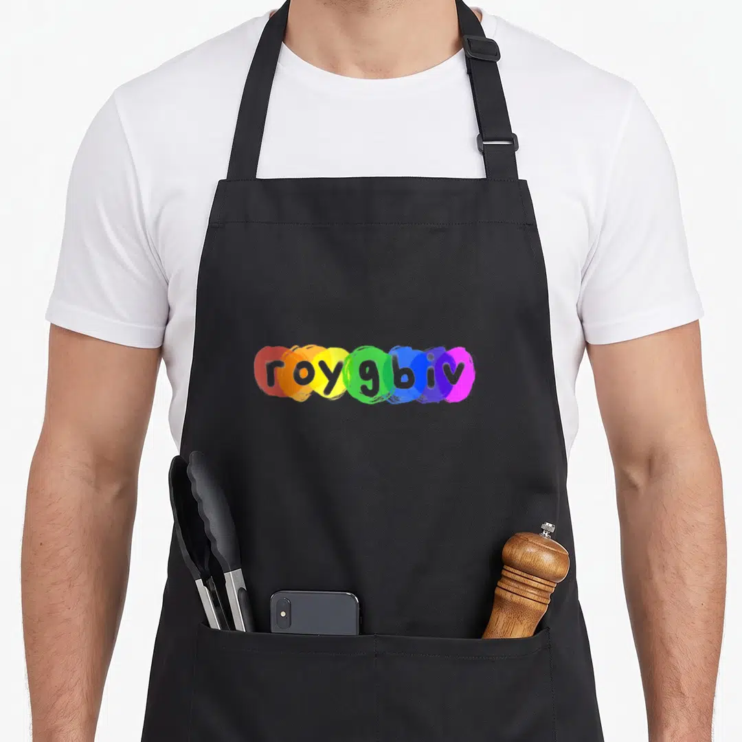 Roygbiv paint apron - Printed roygbiv text over red, orange, yellow, green, blue, indigo, violet paint splashes — shown on a black cotton canvas apron against a white background