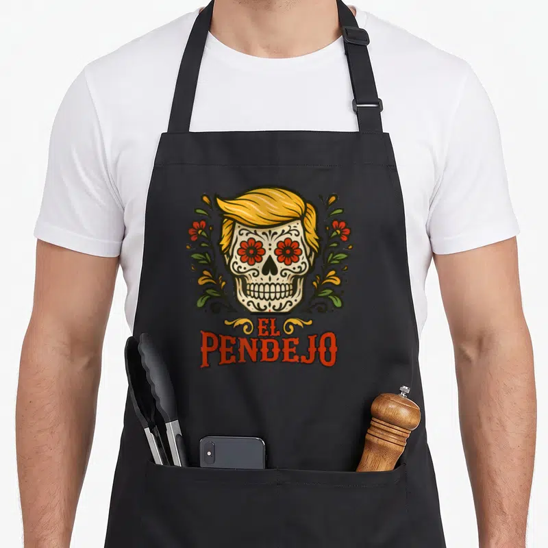 Sugar mexican style apron - Sugar skull with yellow hair, red floral eyes, green vines, and orange El Pendejo text — shown on a black cotton canvas apron against a white background