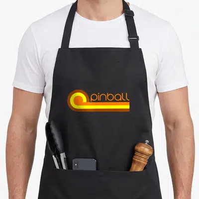 School 70s apron - Retro pinball logo with orange yellow circle and horizontal stripes next to text — shown on a black cotton canvas apron against a white background