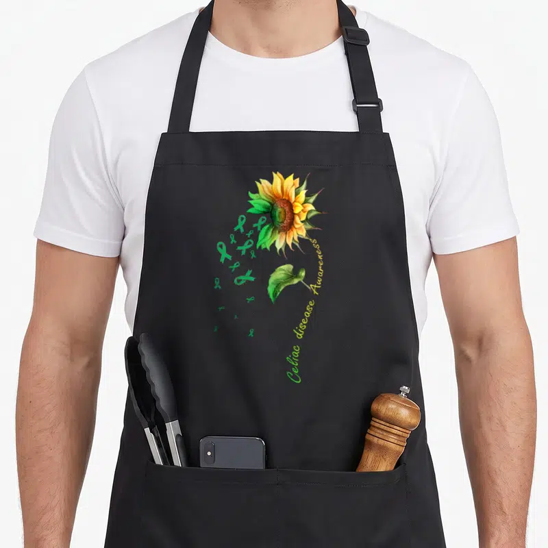 Celiac sunflower apron - Watercolor sunflower with green ribbons and curved Celiac disease Awareness text — shown on a black cotton canvas apron against a white background